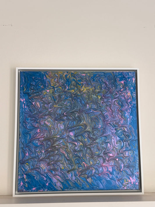 A square framed abstract painting featuring swirling, marbled textures in shades of blue, purple, pink, and hints of gold, displayed against a plain off-white wall.
